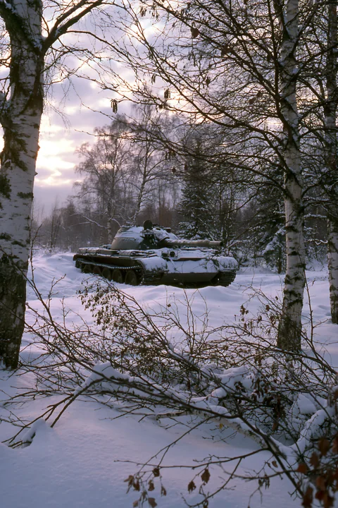 A tank sits in a snowy forest surrounded by trees.
