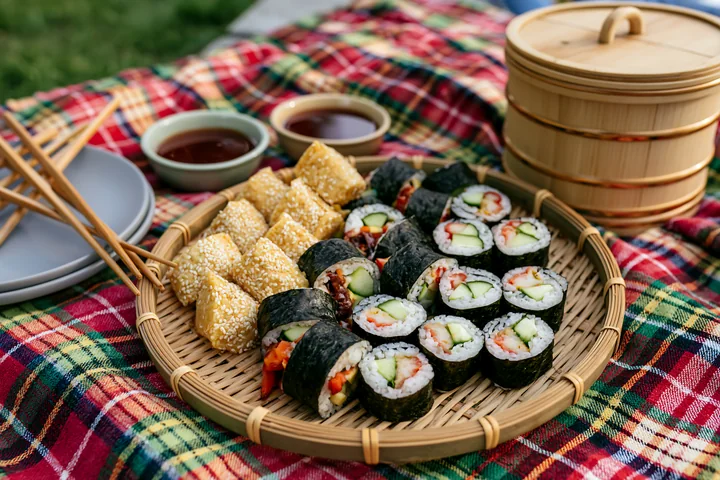 A vegan sushi platter features assorted rolls and fried tofu pieces on a picnic blanket.