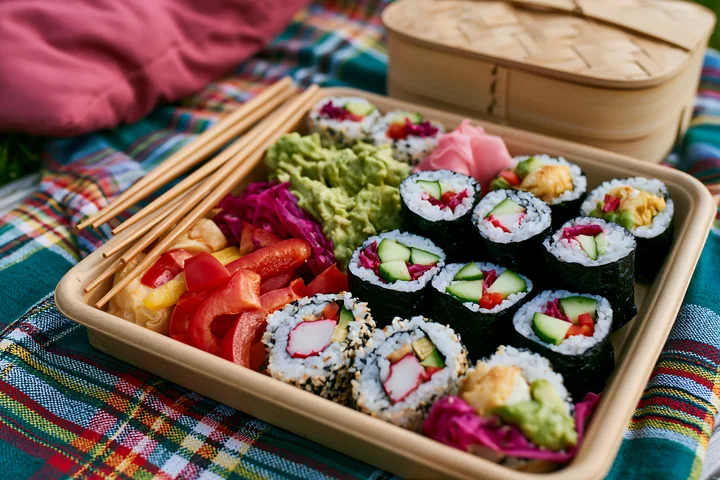 A vegan sushi platter includes various rolls made with vegetables, paired with sauces and fresh toppings.