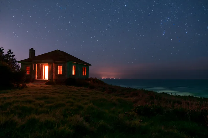 A villa stands on a hillside with lights glowing in the windows under a star-filled sky.