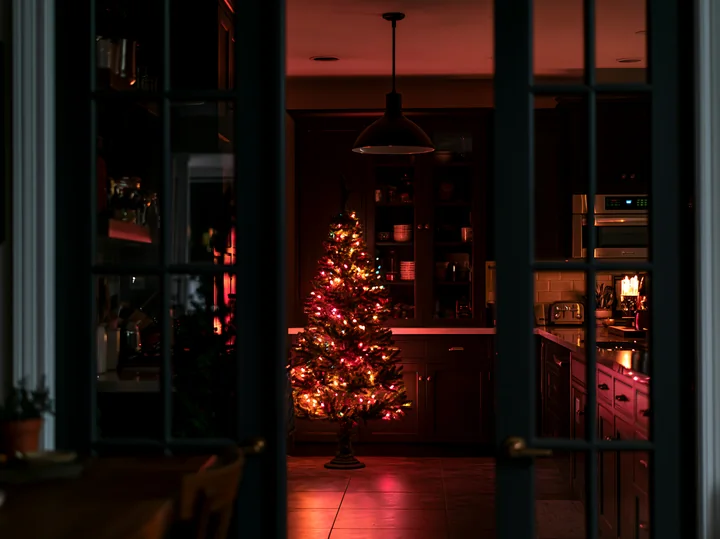 A warm light shines in a modern kitchen where a Christmas tree reflects in the glass doors.