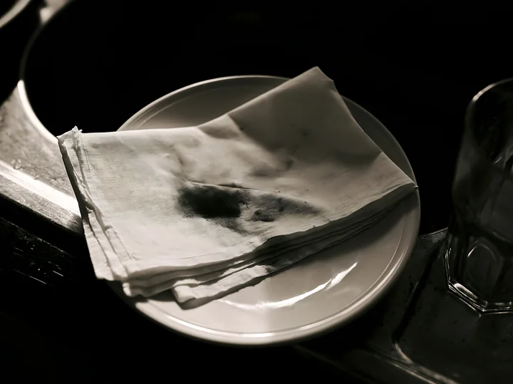 A white textile rests on a plate with visible ink splashes, suggesting a moment of mishap in a dining or crafting setting.