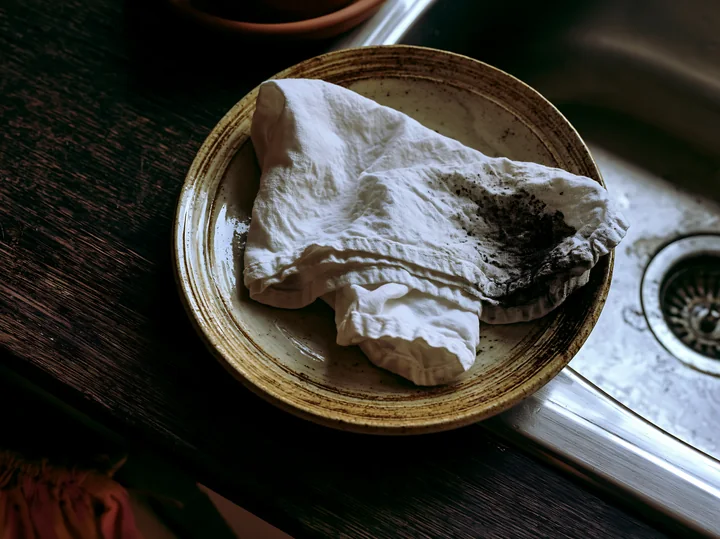A white textile with accidental ink splashes lies on a plate beside a sink in a kitchen.
