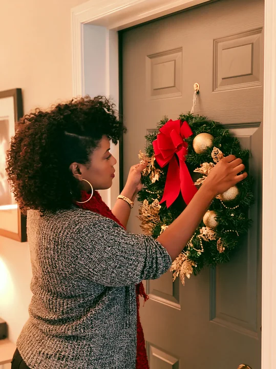A woman decorates her apartment door with a Christmas wreath.