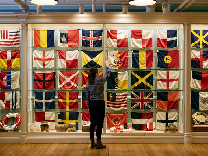 A woman examines a display of historic maritime flags in the lighthouse museum interior.