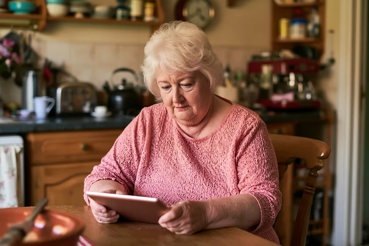 A woman sits at a kitchen table using a tablet.