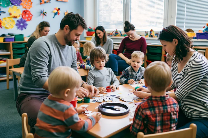 Adults and children make paper snowflakes together at a classroom craft table.