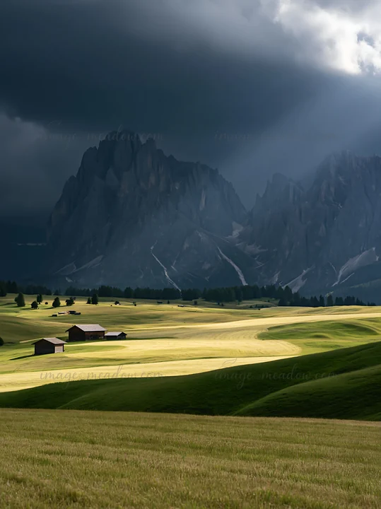 Sunbeams shine down on the Alpe di Siusi meadow. The scene features green grass and wooden structures against a dramatic mountain backdrop.