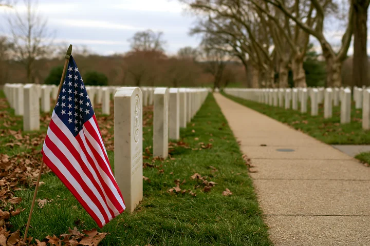 An American flag marks a grave at Arlington Cemetery, surrounded by rows of white gravestones.