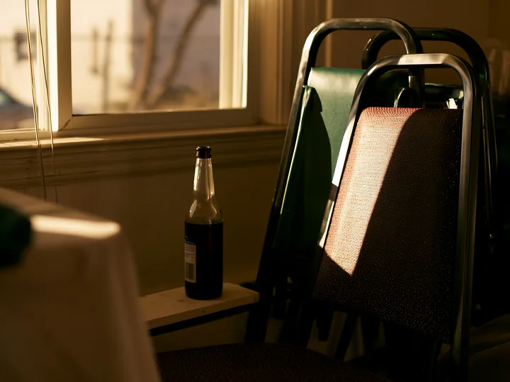 An empty bottle after party sits on a chair in a sunlit room.