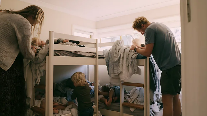 Blonde parents tucking blonde children into bed at home during evening time.