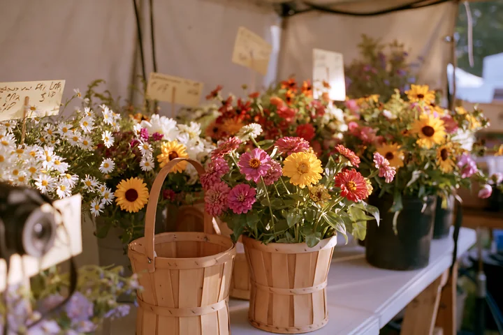 Brightly colored flowers are arranged in wooden baskets at a farmers market.
