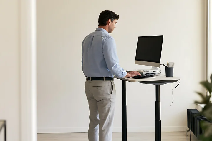 Businessman stands alone at a computer desk in a bright minimalist office.