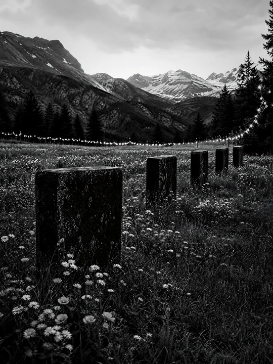 String lights illuminate a meadow nestled in a mountain valley. The scene captures the contrast of the lights against the darkening sky and silhouettes of mount