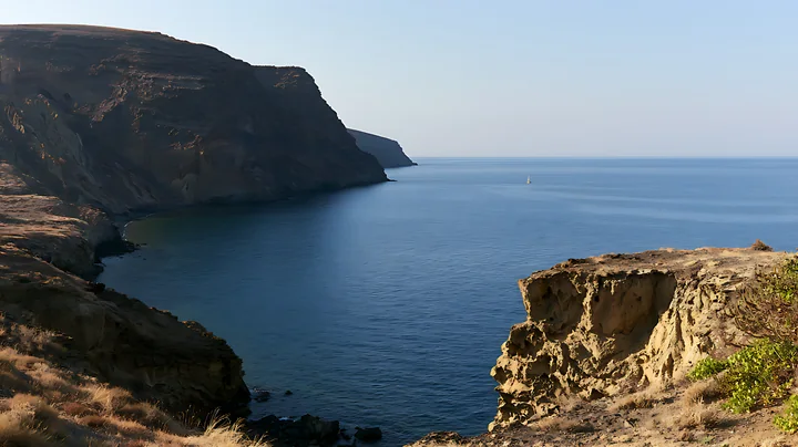 Coastal cliffs overlook the calm ocean waters under a clear blue sky.