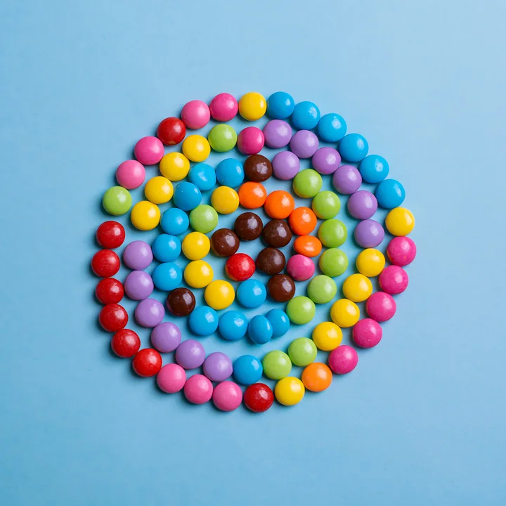 Colorful candy pieces forming spiral create a vibrant design against a blue background.