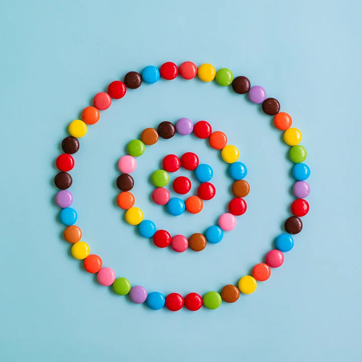Colorful candy pieces forming spiral create a visually appealing pattern on a blue background.
