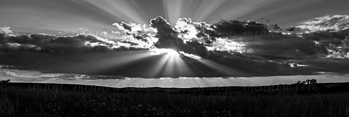 Sunlight breaks through clouds, casting rays across a vast meadow. The scene shows the sky filled with clouds while the ground is mostly bare, depicting a natur