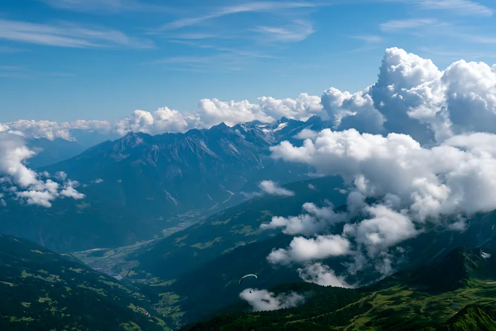 Dramatic clouds around alpine peaks fill the sky above green valleys.