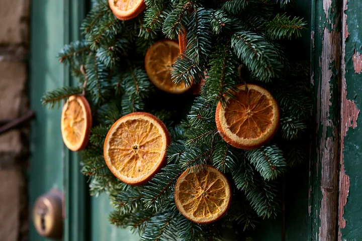 Evergreen Christmas wreath decorated with dried orange slices hangs on a weathered green apartment door.