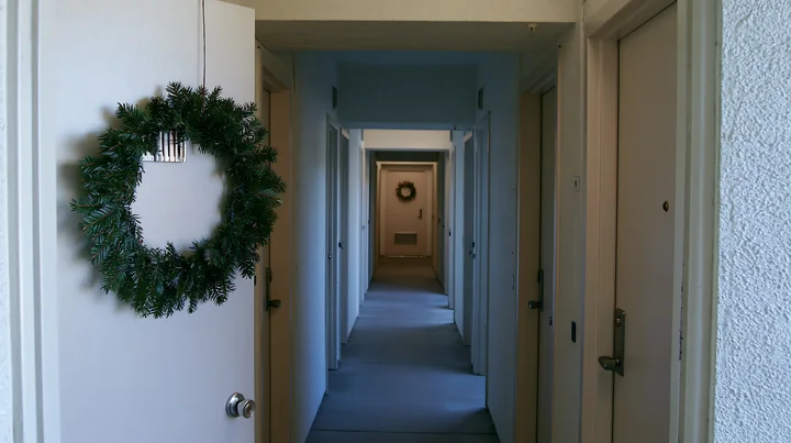 Evergreen Christmas wreath hangs on an apartment door beside a long residential hallway.