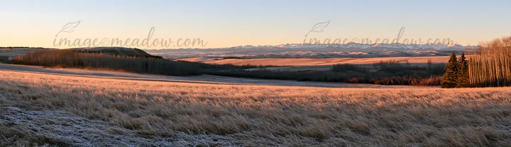 A frosty meadow shows grass covered in frost as the sun rises. In the background, the mountains are visible under a clear sky. The scene captures the early morn