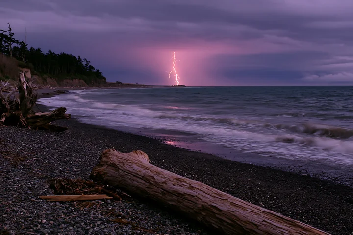 Lightning strikes the ocean near the coastline, illuminating the dark sky.