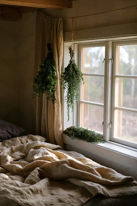 Natural light shines through the window onto linen bedding in a rustic bedroom.