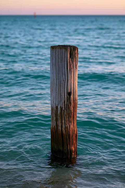 Old wooden piling against a turquoise horizon shows the structure standing in clear water.