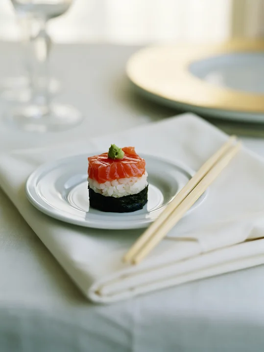 One salmon maki piece with wasabi is placed on a small white plate.