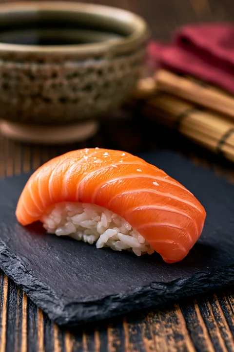One salmon nigiri on slate plate sits on a wooden table.