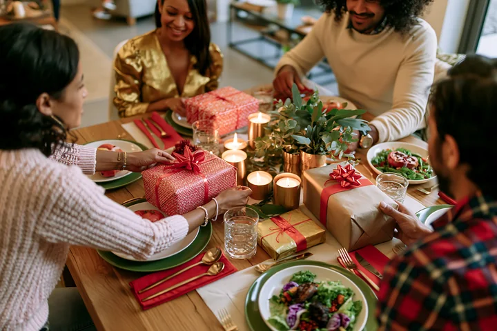 Parents are seen placing gifts on a dining table set with plates and decorations.