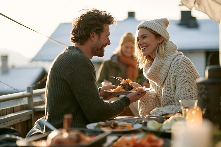 Parents serve a festive meal to each other at an outdoor table in winter clothing.