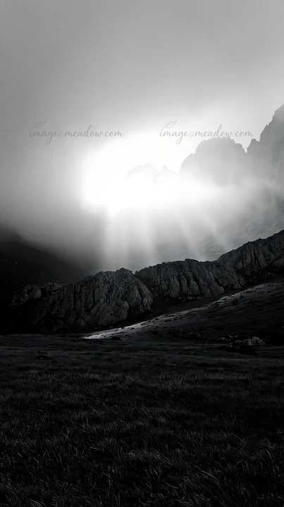Rays of sunlight shine through clouds in the Picos de Europa mountain range. The scene captures grass and rocky terrain under a dramatic, cloudy sky during dayt