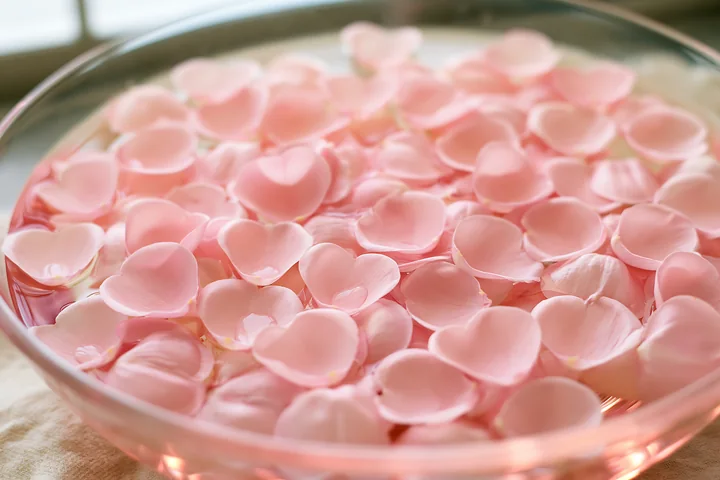 Pink heart-shaped flower petals are floating in a clear bowl of water, creating a visually appealing scene.