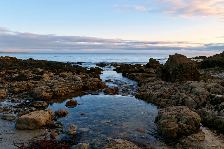 Rocks line the shoreline where water flows into a small pool.