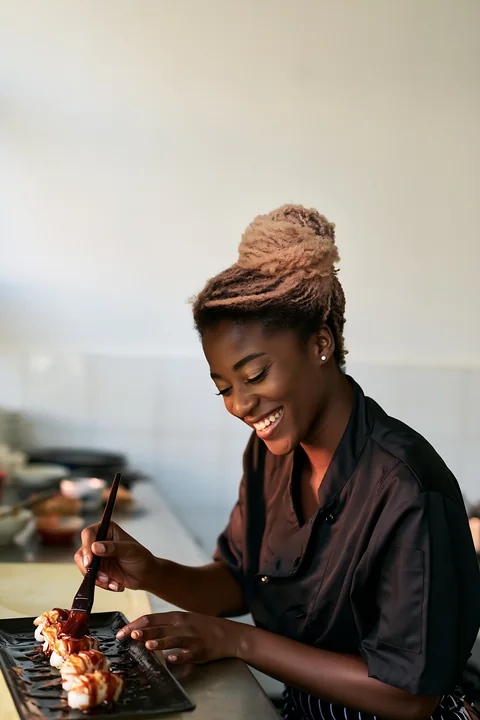 Smiling sushi chef brushes sauce onto sushi pieces at a counter with generous blank copy space.