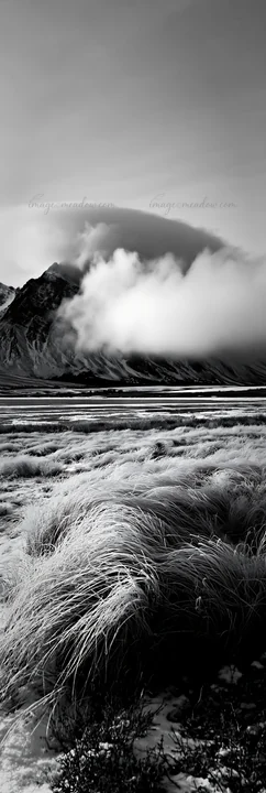 Snow covers a meadow near a lake. Mountains rise in the background, partially hidden by clouds. The scene captures a quiet winter afternoon in a remote area.