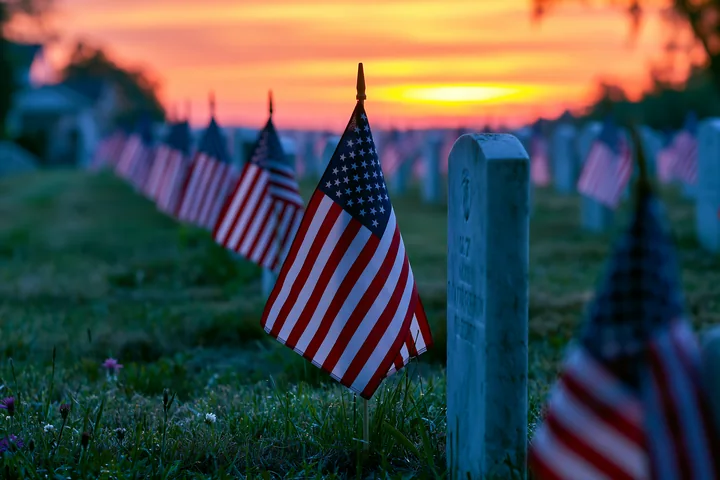 Sunrise lights up a military cemetery with rows of headstones and American flags.