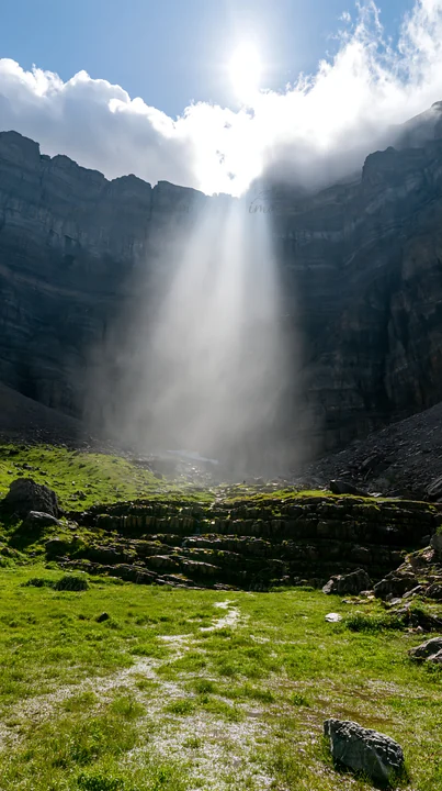 Light rays come through clouds and illuminate a rocky area in Sunshine Meadows, Banff. The green grass contrasts with the rugged mountains, creating an engaging