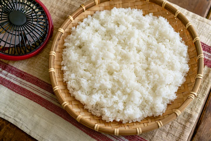 Sushi rice cooling on a bamboo tray sits on a table.
