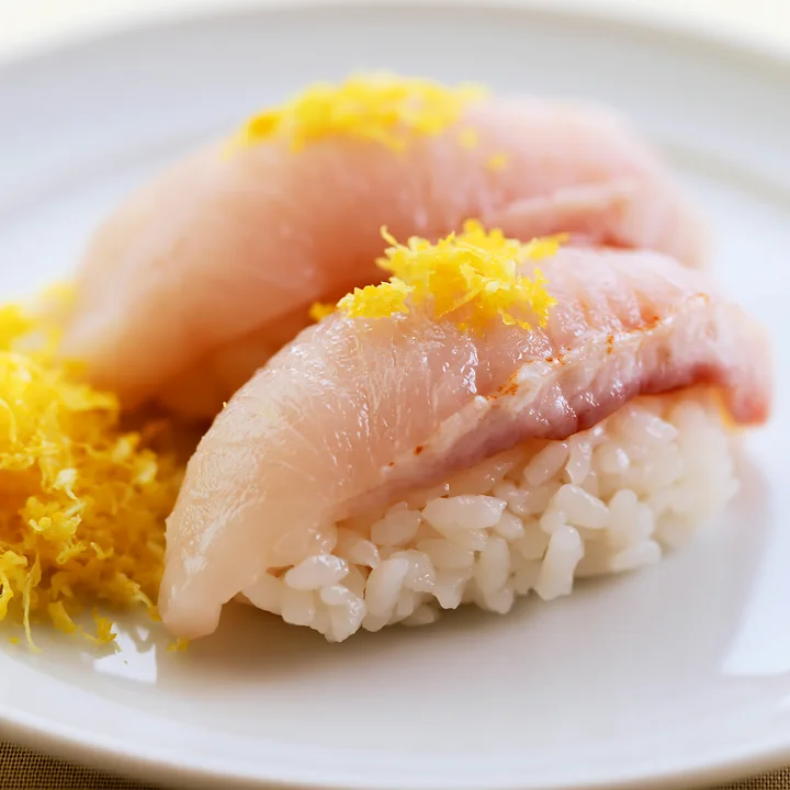 Sushi with lemon garnish close-up showcases two pieces of sashimi on rice, neatly arranged on a round white plate.