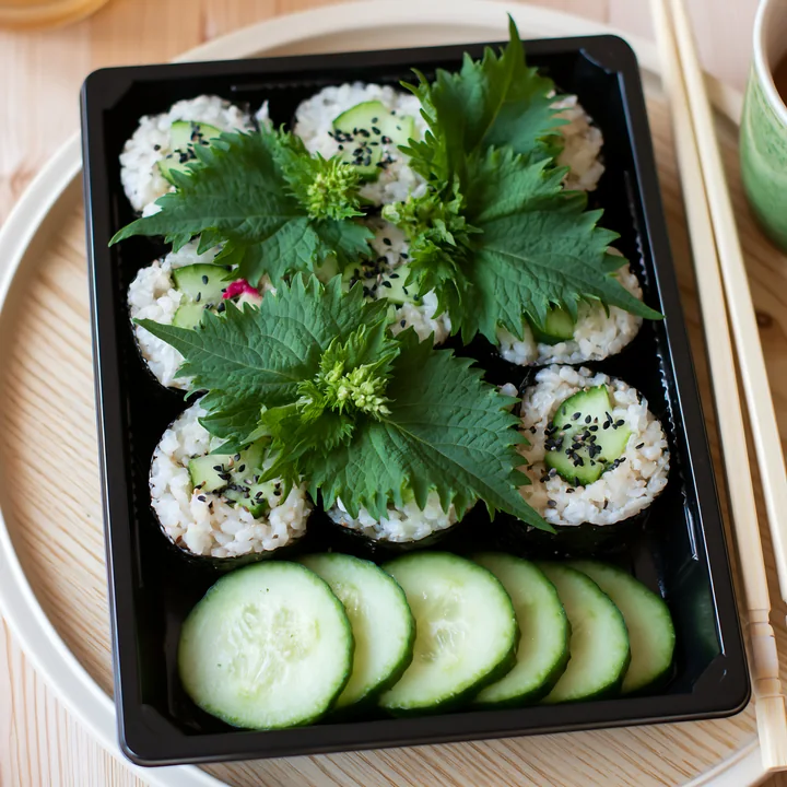 Sushi with shiso leaves is arranged neatly in a black tray with cucumber slices.