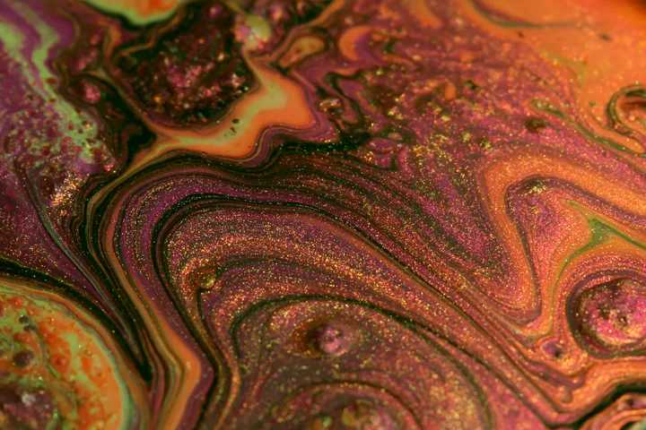 The photograph shows a colorful abstract swirl glittering pattern featuring vibrant hues and shimmering effects on a smooth surface.