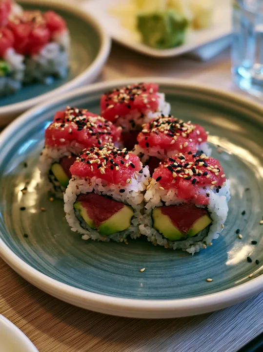 This close-up shows a plate of sushi with spicy tuna rolls topped with sesame seeds.