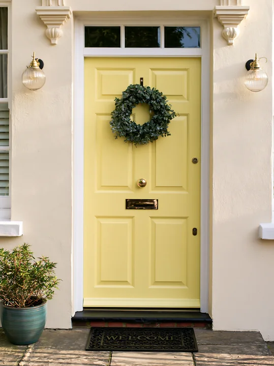 This door features a yellow color with a green wreath and a welcome mat, set against a light neutral exterior.