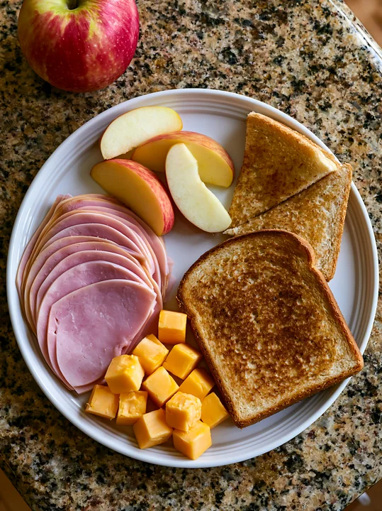 This plate features cold cuts, cheese cubes, sliced apples, and toast.