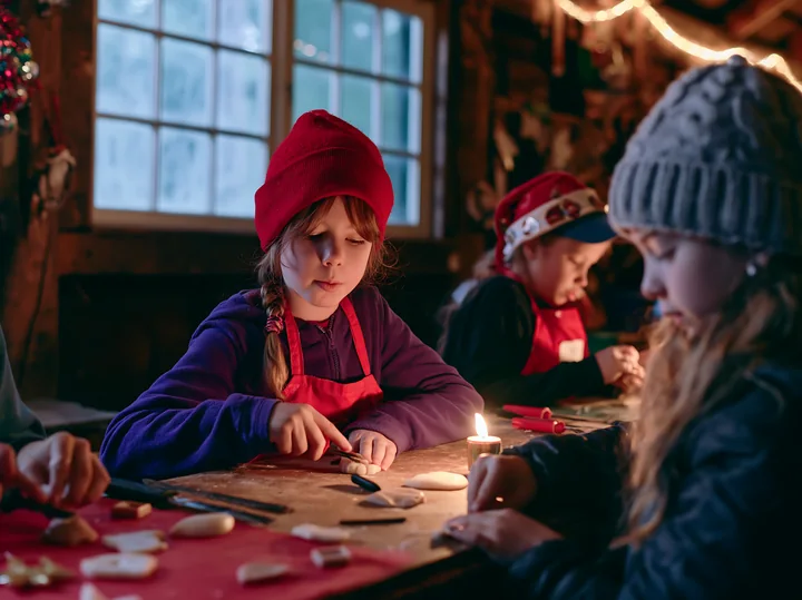 Three children make handmade ornaments at a warmly lit holiday craft table.