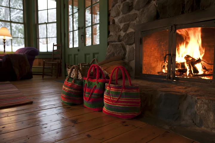 Three colorful shopping bags sit beside a stone fireplace in a cabin.