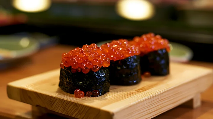 Three pieces of ikura salmon roe sushi sit on a wooden tray.